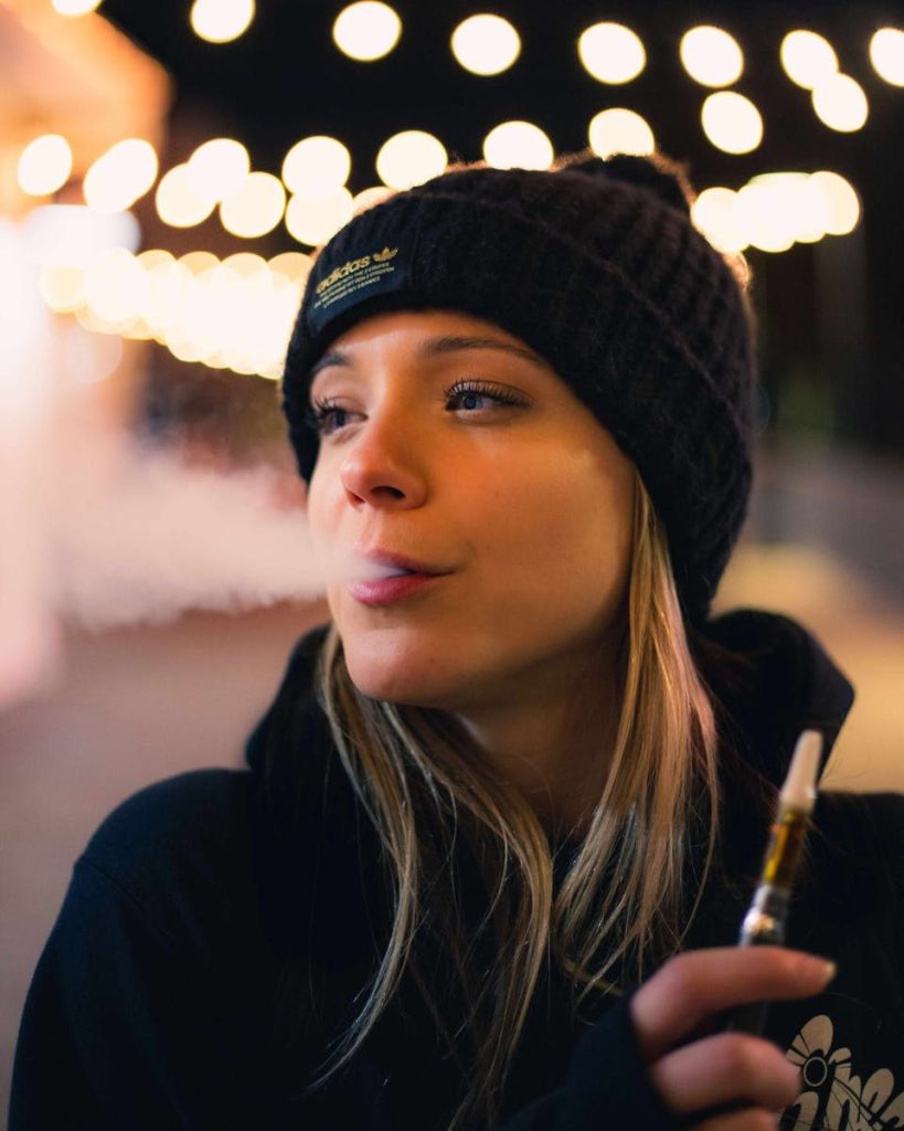 Young woman enjoying vaping at night with city lights in the background, Sacramento, CA.